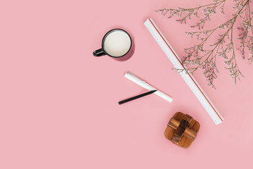 Pink color background with flower branches, scale ruler, a cup of milk, pen, pencil and wooden block on the right side. Architect and designer background with copy space.