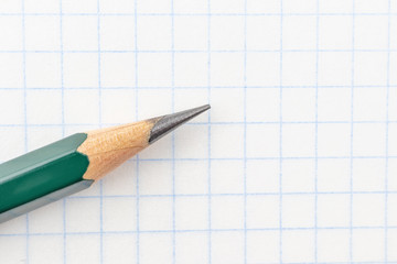 The concept of preparation for school. Slate pencil closeup on notebook sheet in a cage. Background image for training topics, school lessons. Place for text.