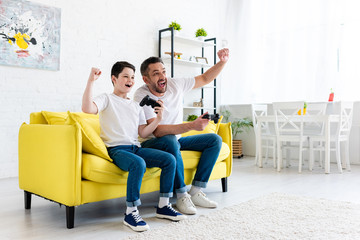 excited father and son cheering while playing Video Game on couch at home © LIGHTFIELD STUDIOS