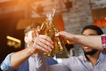 Male Friends Drinking Beer And Clinking Bottles At Bar