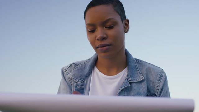 Young black female artist drawing on a sketchpad outdoors in teh countryside
