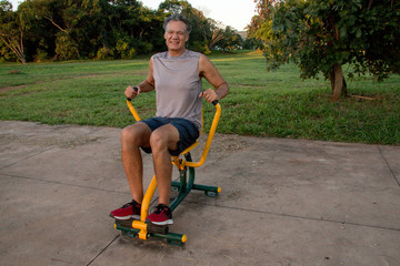 Fit Middle Aged Mature Man Working Out on a Rowing Machine at a Outdoor Fitness Park