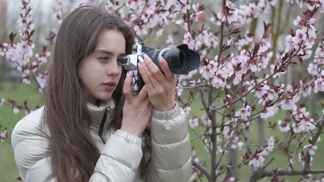 A young girl takes pictures in nature. A young girl photographs a blossoming tree.