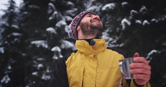 Smiling young guy in the middle of amazing snowy forest , he are very elated of all the landscape he see , by the way he get warm with a cup of tea