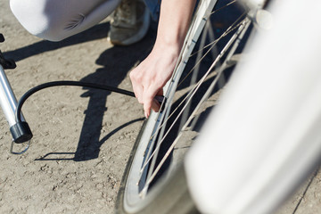 Obraz premium Young beautiful girl trying to pump up the wheel of the bike. A girl holds a pump in her hands and tries to pump up. The girl repairs a bicycle on the street
