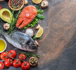 Raw dorado fish and salmon steak with spices and vegetables on the graphite board.
