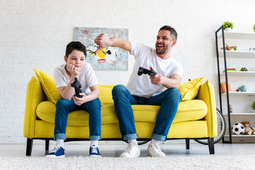 father showing thumb down while sitting with son and playing Video Game at home