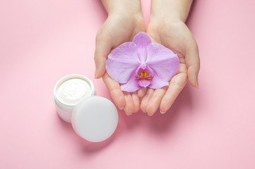 Obraz na płótnie Canvas Mockup for hand skin care natural cosmetics. Woman hold orchid flower in hands on a pink background. Natural organic cosmetics with flowers extract. Beauty, fashion, cosmetology and spa concept.