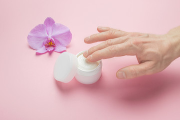 Man herbal body care cosmetic mockup. Man hands applying moisturizing cream to him skin. Natural organic cosmetics with flowers extract. Copy space, pink background. 