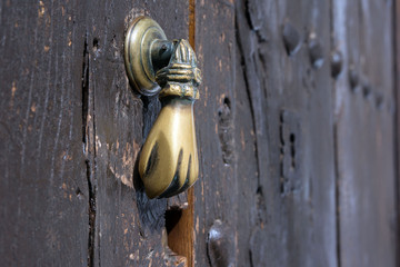 Old bronze door handle in the shape of a hand. Brown wooden door of a house in the Spanish city of...