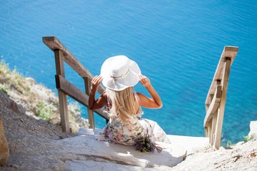 girl in a white hat sitting on the stairs on the shore of the turquoise sea