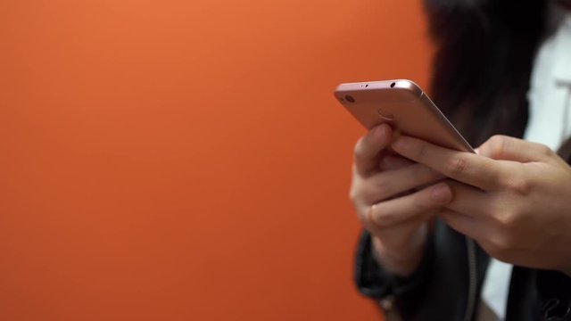 Young woman holding mobile phone in hand on orange background. Female typing a message on a smartphone