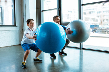 father and son doing squats with fitness balls at gym