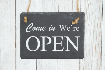 Come in we're Open text on a hanging chalkboard on weathered whitewash textured wood