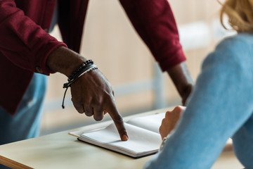 partial view of african american student pointing with finger at notebook