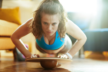 sports woman in modern house doing pushups using balance board