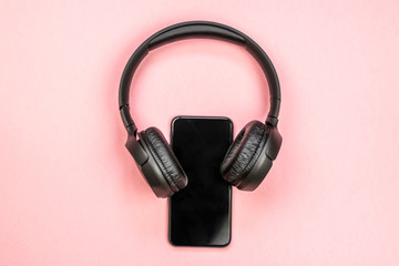 Close-up of smart phone with headphones on a pink background. (Top view). Listen to music.