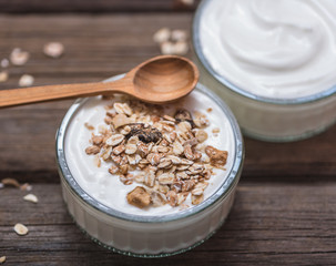 White yogurt in glass bowl on old wooden desk with wooden spoon on the top side.