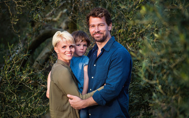 Young family with two small daughter standing outdoors by olive tree.