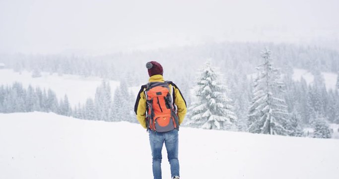 Walking tourist in the snowy forest equipped with all travel stuff , with a big orange bag , he travel in the middle of mountain