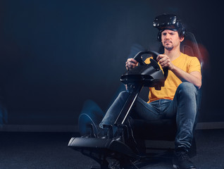 Obraz na płótnie Canvas Man dressed in yellow shirt and jeans wearing VR headset driving on car racing simulator cockpit with seat and wheel.