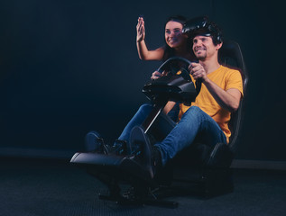 Man driving on car racing simulator while his girlfriend cheering him. Attractive couple having fun together.