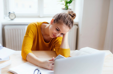 A young female student sitting at the table, using smartpone when studying.