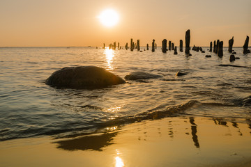 Sunset over the Baltic Sea. Reflection in the wet sand of an old ruined pier. Low sun