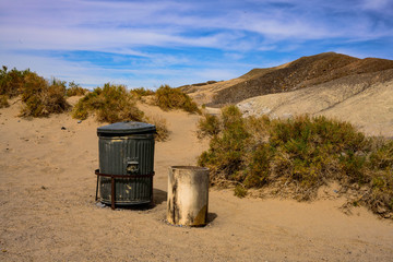 Old garbage bins in the desert park with dry grass over sand dune mountains blue sky background