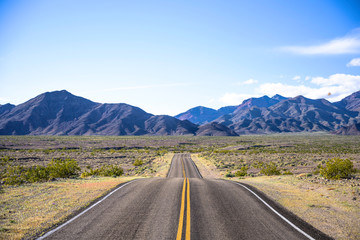 Fototapeta premium Beautiful landscape of Long straight road with yellow line way to the mountains over blue sky summer holiday time at Death Valley USA.