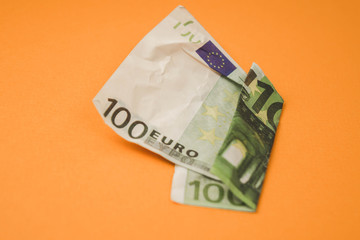 Obraz premium zmięte sto euro leżącego na pomarańczowym tle