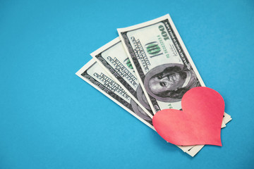 Red heart shape and 100 dollar bills on blue background.
