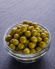 canned green peas in a glass bowl on a dark stone background