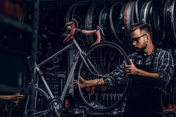 Handsome serious man in protective glasses is fixing bicycle at his own shop.