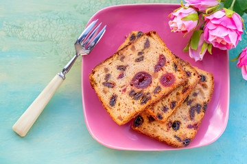 Pastries. A cake slice with fruits on a pink plate. Fruit cake raisin and cherry.
