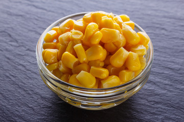 canned corn in a glass bowl on a dark stone background
