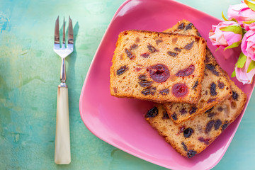 Pastries. A cake slice with fruits on a pink plate. Fruit cake raisin and cherry.