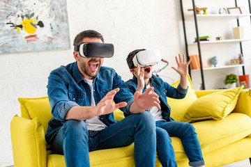 excited father and son in vr headsets experiencing Virtual reality on couch at home