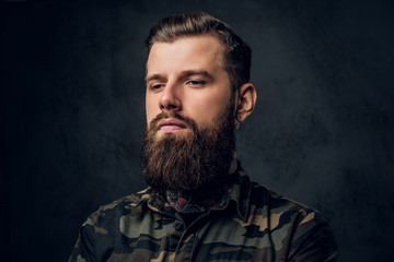 Closeup portrait of a young tattooed man with beard and hairstyle. Studio photo against a dark wall
