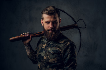 A bearded tattooed hipster guy in military shirt posing with a medieval crossbow. Studio photo...