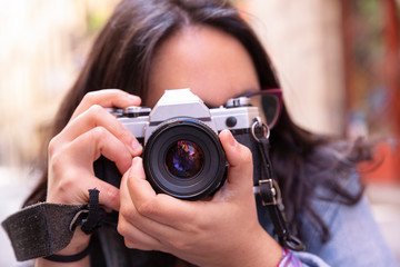 Retrato del rostro de mujer joven sujetando con sus manos una preciosa cámara de fotos analógica en la calle 