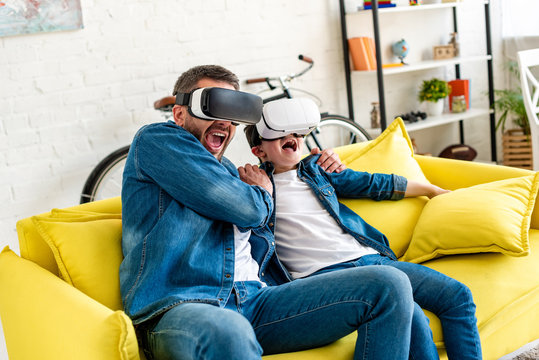 father and son in vr headsets yelling while experiencing Virtual reality on couch at home