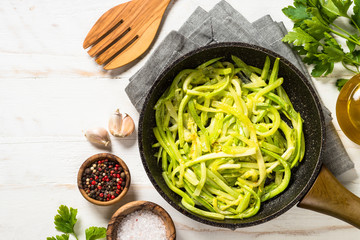 Zucchini noodles in frying pan on white.