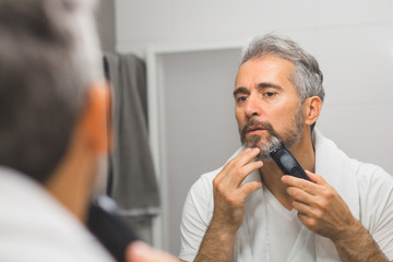 middle aged handsome man trimming his beard in bathroom