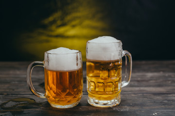 cold tasty beers in mugs on dark wooden background