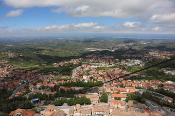 Fototapeta na wymiar panoramic view from top of Fortress Guaita on Mount Titano on city San Marino ,Italy with beautiful blue sky with clouds on sunny day. View towards the sea and over the San Marino villages and Rimini,