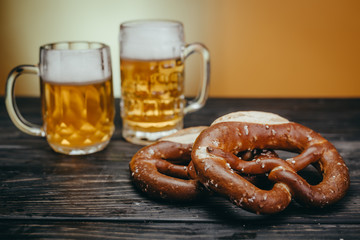 draft beer in the mugs and pretzels on wooden board against yellow background