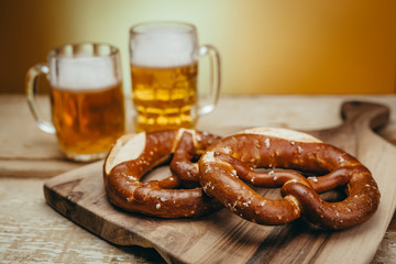draft beer in the mugs and pretzels on wooden board against yellow background