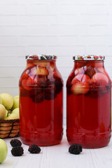 Compote of berries and apples in jars on a table on a white background, on the table there apples, blackberries. Free place for the inscription
