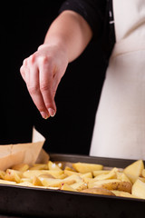 young woman in apron seasoning salt potatoes